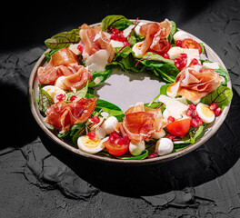 Fresh salad with greens, cheese, and prosciutto on a dark table
