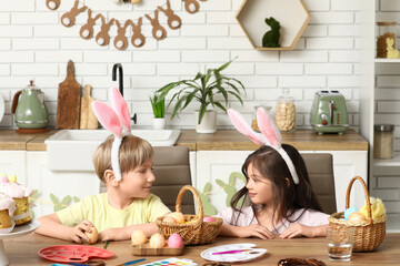 Cute little children with bunny ears and painted Easter eggs at home