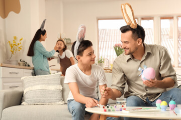 Little boy with his father in bunny ears painting eggs at home on Easter Day