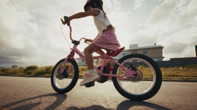 Pre teen caucasian girl rides a pink bicycle on a quiet road wearing a safety helmet. First bicycle ride. Girl learns cycling on a street