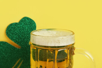Mug of beer with paper clover on yellow background. St. Patrick's Day celebration