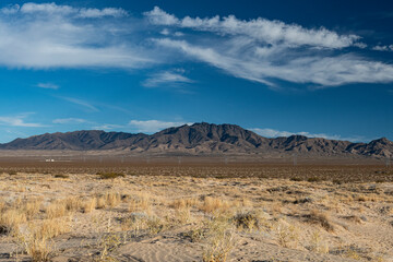 A vast desert landscape showcasing rugged mountains against a brilliant blue sky with scattered clouds, highlighting the beauty of arid environments and natural vistas.