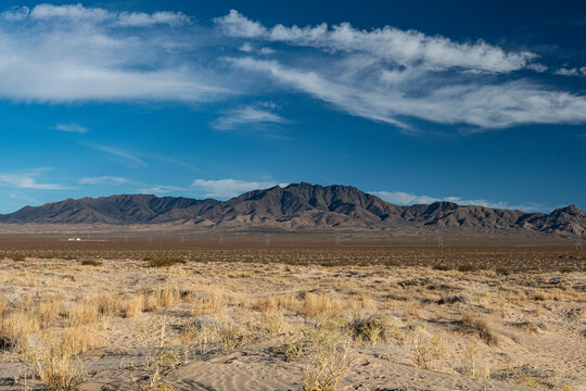 A vast desert landscape showcasing rugged mountains against a brilliant blue sky with scattered clouds, highlighting the beauty of arid environments and natural vistas.