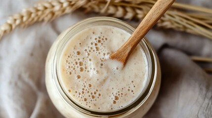 Top view of glass jar with sourdough starter and wooden spoon on linen fabric. Homemade bread baking