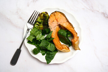 Enjoying delicious grilled salmon served with fresh greens, perfect for healthy meals and diets on white aestetics plate on marple background.
