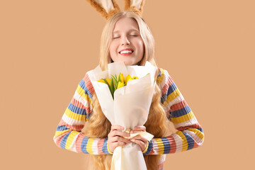 Young girl with Easter bunny ears and flowers on beige background