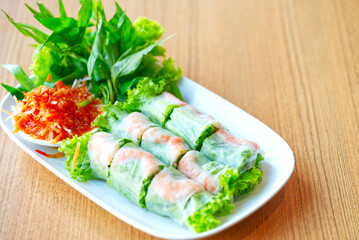 Vietnamese food, fresh spring rolls with fresh vegetables, prawns dipping with sweet chili sauce on a wooden table, natural light, space for copy.