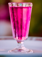 Glass of pink liquid is sitting on a white plate