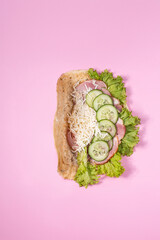 Taco filled with shredded cheese, slices of cucumber, and green leaf lettuce, placed on pink background. The taco shell appears soft and is partially visible, with ingredients arranged neatly.