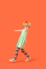 Funny girl in clown costume on orange background. April Fool's Day celebration