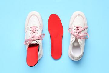 Sneakers and red orthopedic insoles on blue background