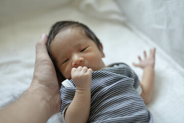 A baby is laying on a white sheet with its arms outstretched. The baby has a black and white striped shirt on
