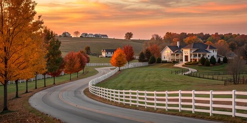 Fototapeta premium Winding Gated Road with Pristine White Fence at Sunset on a Crisp Autumn Evening, Leading to Luxury Homes on Sprawling Acreage in a Picturesque Rural Landscape