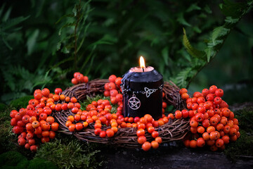 burning magic black candle with pentacle amulet and rowan tree berries in forest. Magic,...