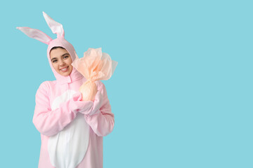 Beautiful young woman in bunny costume with Easter gift egg on blue background