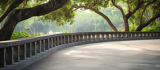 Serene concrete pathway winding through a lush green park with artificial tree branch railing on the left and sunlight filtering through trees above.