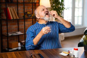 Retired Indian senior man takes his daily dose of medicine or pill for health while sitting at home