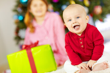 Baby, portrait and gift box by Christmas tree in home, playful and happy with party in living room. Infant, child and present with holiday, smile and festive celebration at family house in Australia