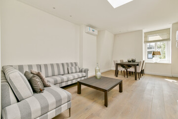 Fototapeta premium A stylish minimalistic living room featuring striped sofas and a wooden table. natural light filters through a large window, enhancing the serene atmosphere.