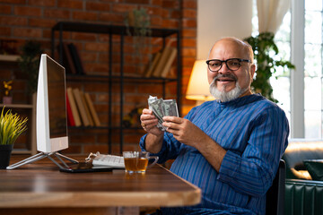 Indian elderly man counting five hundred rupee notes while sitting at his desk at home