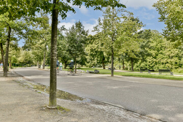 A peaceful park scene featuring a paved pathway lined with trees, offering a glimpse of nature's tranquility and greenery amidst an urban setting.