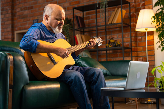 Senior Indian man with a beard practicing guitar at home while following an online tutorial
