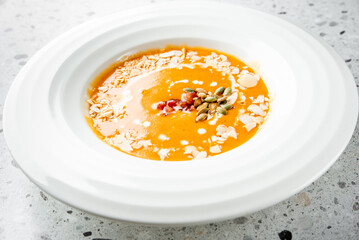A creamy orange soup garnished with slivered almonds and pumpkin seeds, served in a stylish white...