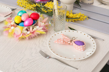 Easter table setting with mimosa flowers, tableware and painted eggs
