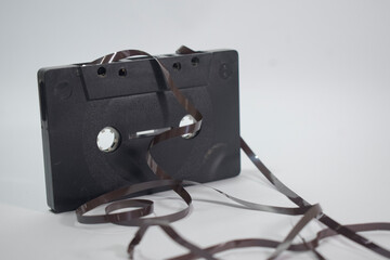 stock photo of technology; black Old cassette with unwound tape isolated on white background.: cassettes were a very popular sound recording medium in the 80s to late 90s.