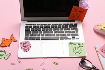 Laptop and sticky notes on pink background. April Fools Day prank
