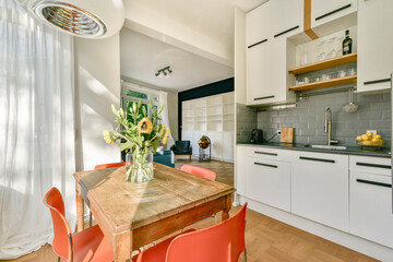 A stylish kitchen featuring a wooden dining table surrounded by bright chairs, complemented by natural light and modern furnishings.