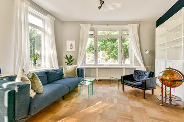 A beautifully designed living room featuring a blue couch, glass tables, and large windows allowing...