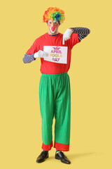 Portrait of clown pointing at poster with text APRIL FOOLS DAY on yellow background