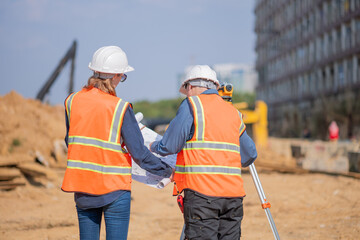 Construction surveyor or engineer working construction site blueprint and theodolite mounted tripod...