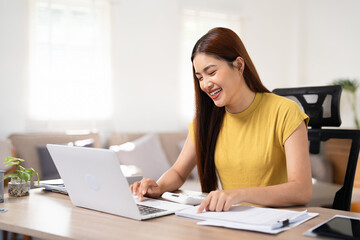 Obraz premium Smiling Asian Businesswoman sitting and working hard with computer and lots of documents on the table in living room at home.