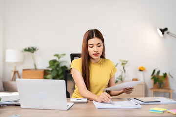Business woman, female entrepreneur using calculator during online working on laptop computer on office table at home, telecommuting, work from home concept