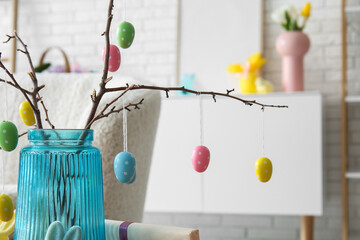 Tree branches with color Easter eggs in glass vase in interior of living room, closeup
