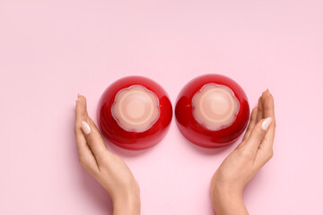 Female hands and ceramic bowls with silicone nipple covers on pink background, closeup. Erotic and female health care concept