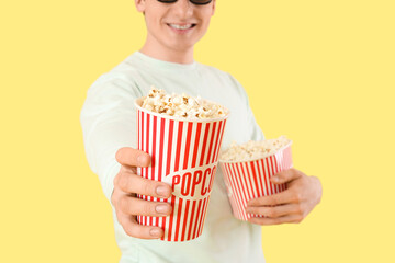 Young happy man in 3d eyeglasses with popcorn buckets on yellow background
