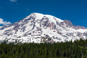 Fototapeta premium This stunning image of a snow-capped mountain showcases the sheer beauty and majesty of nature, contrasting sharply with a clear blue sky and surrounding greenery below.