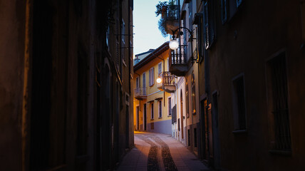 Fototapeta premium Narrow cobblestone street in Verbania Italy illuminated by street lamps at dusk