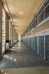 A long, empty corridor inside a modern prison building, featuring multiple cells with barred windows and bright lights, highlighting the building's architectural design and purpose.