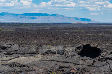 An expansive view of barren lava fields stretching under a beautiful sky, showcasing the stark contrast between harsh geological formations and serene natural beauty.