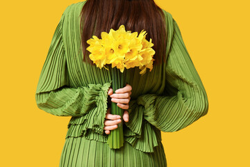 Beautiful young woman with bouquet of beautiful narcissus flowers on yellow background, back view