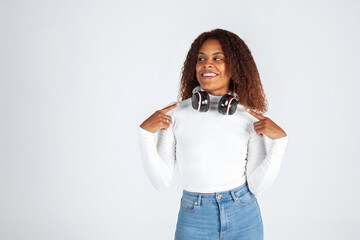 chica negra afroamericana señalando los auriculares, vestida de vaquero y camiseta blanca. Oferta, música, DJ, cursos online, publicidad