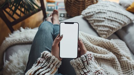 Top view mockup of a woman holding a smartphone with a blank white screen in a cozy bedroom setting