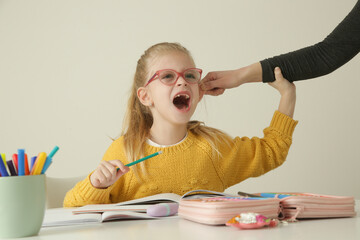 Disobedient little girl being punished by ear pulling while doing homework	