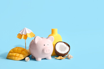 Piggy bank, decorative umbrella, seashells, sunscreen, mango and coconut on blue background