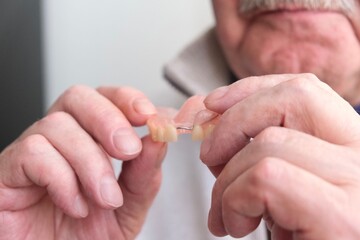 An elderly man holds a denture in his hands. The concept of stomatology and prosthetics. A dental prosthesis. Dentures on hooks