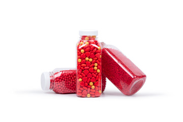 Three transparent plastic bottles filled with vibrant red and gold sprinkles, heart-shaped candies, and sugar pearls, isolated on a white background for baking and cake decorating.